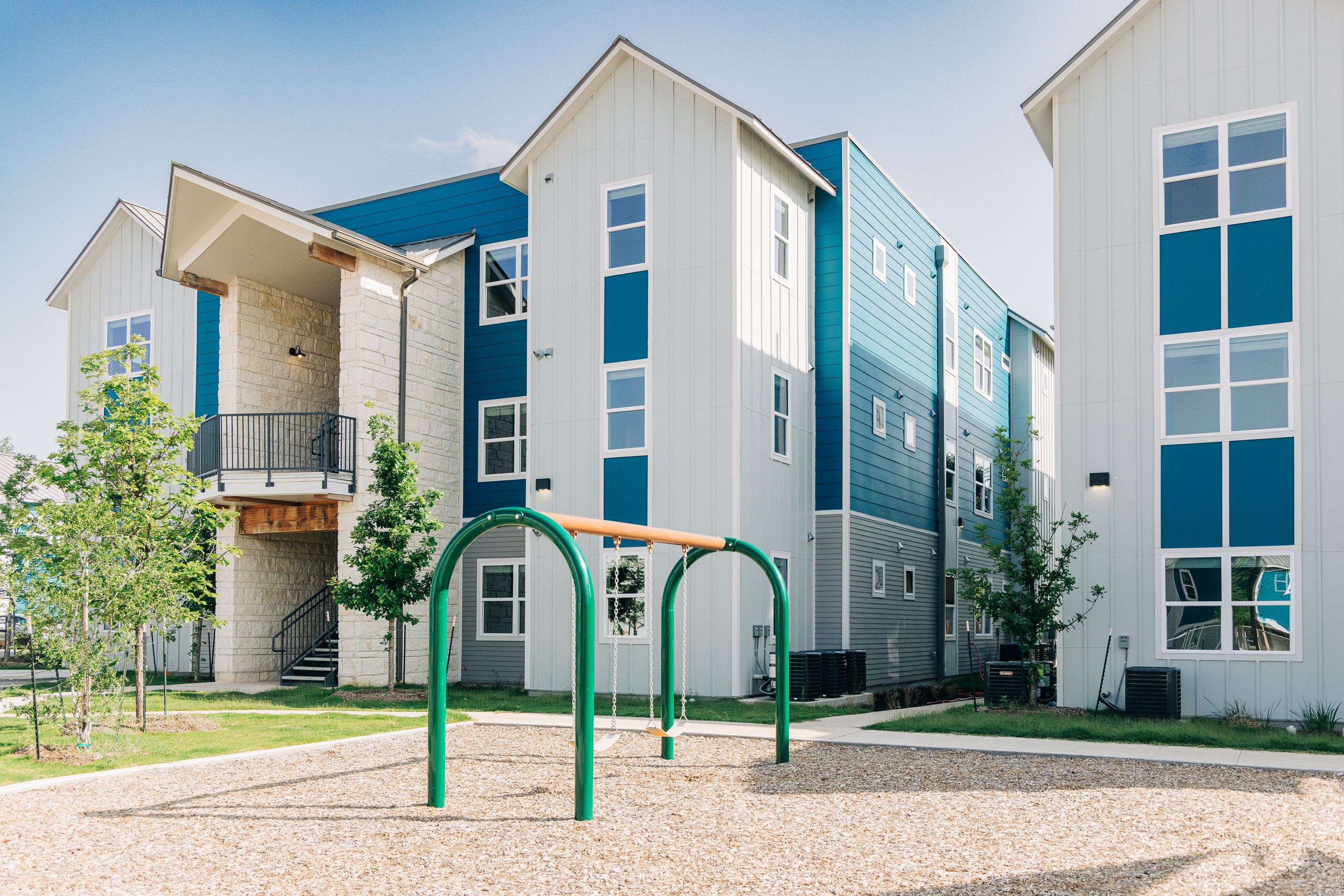 A children's playground in front of Habitat for Humanity apartments with swings. 