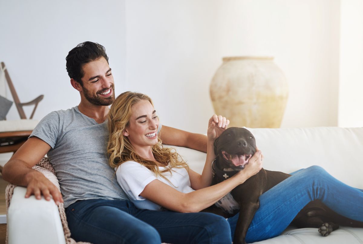Couple laying down in their couch with their dog. 